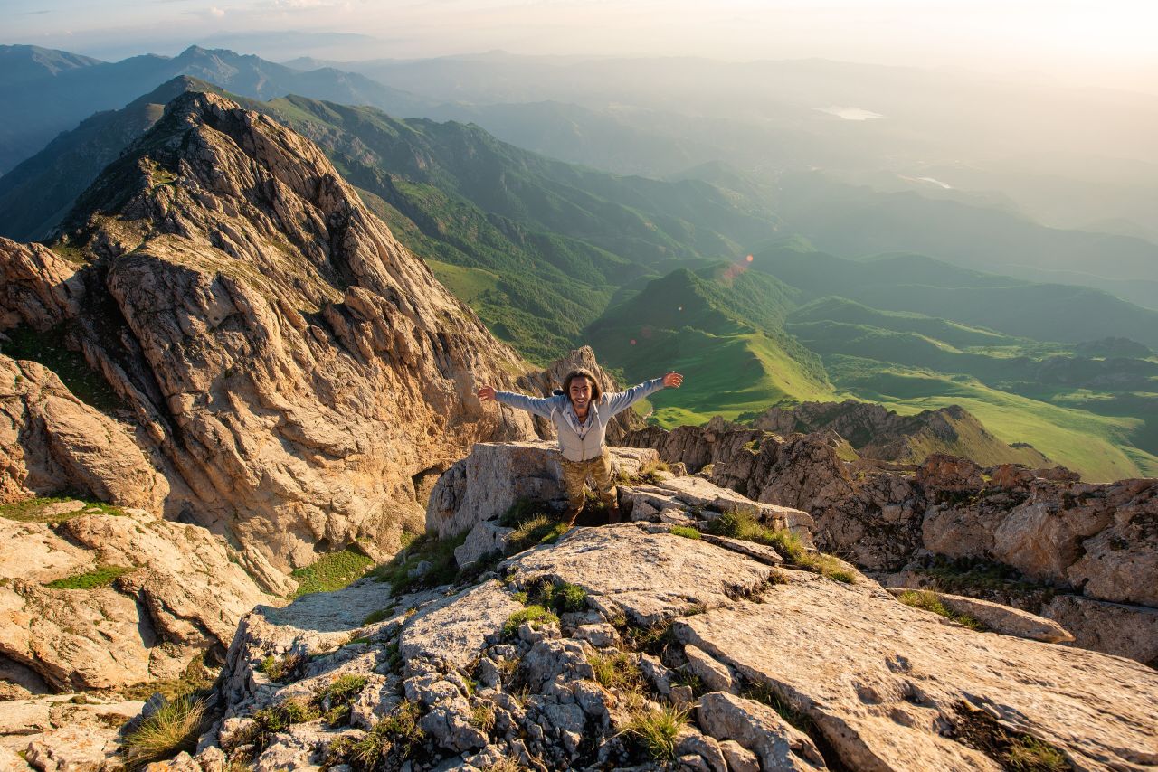 A hiker with arms wide open on the summit of Khustup at sunrise
